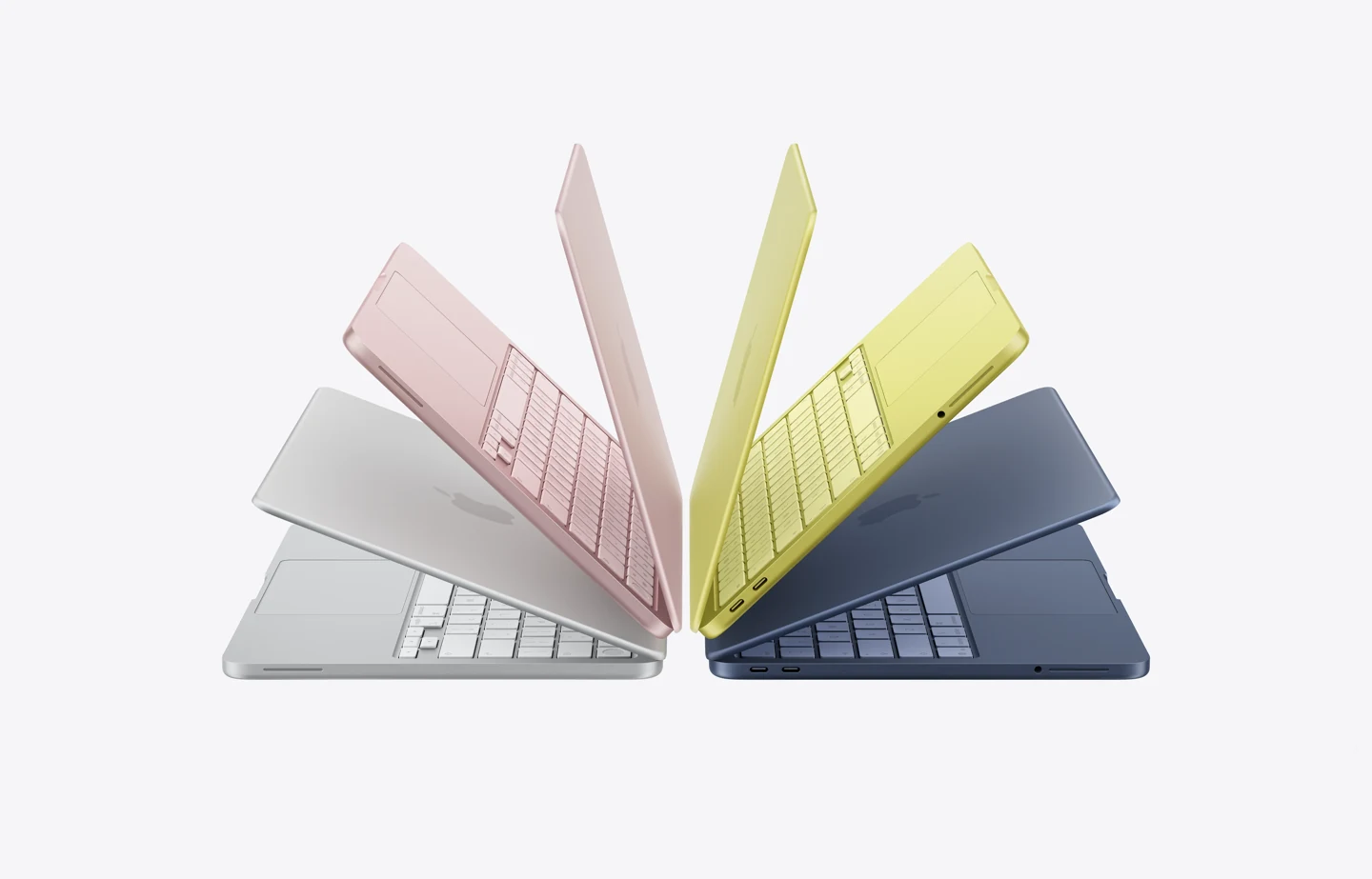 Notebooks MacBook Neo nas cores disponíveis: prateado, blush (rosa-claro), amarelo-cítrico (amarelo brilhante), índigo (azul-escuro), com estrutura de alumínio e tampas parcialmente abertas revelando teclados na mesma cor. Os notebooks estão dispostos em arco para criar o efeito de um livro aberto